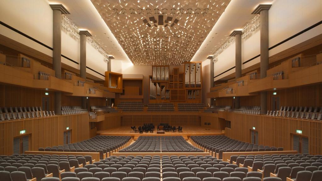 The wooden interior of the Kyoto Concert Hall, with an organ, rows of seats and a perforated ceiling