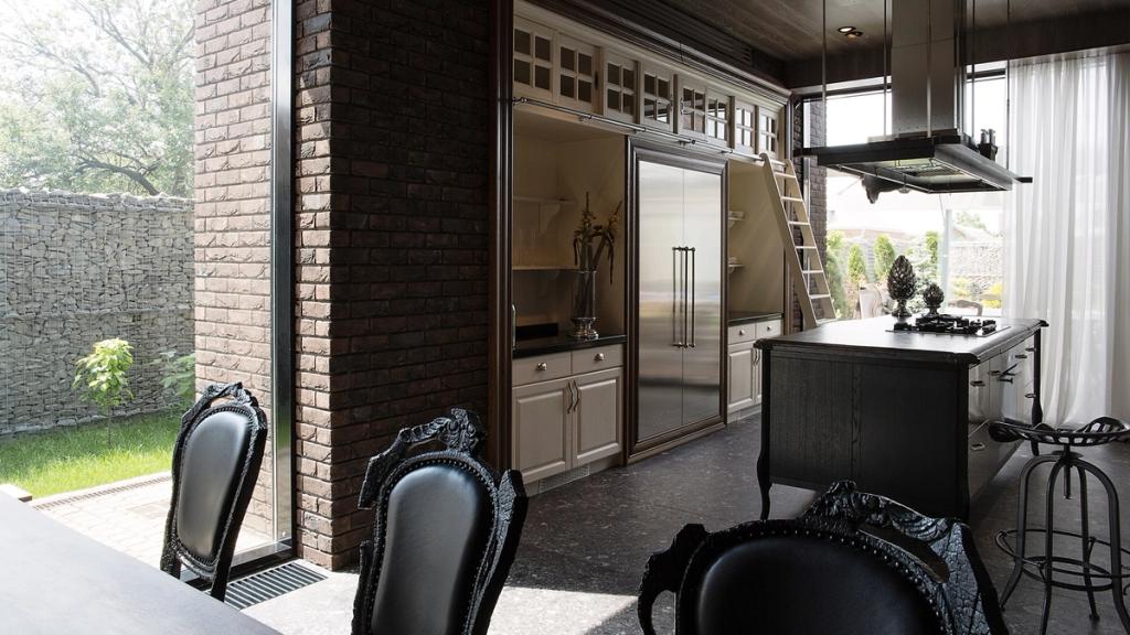 A kitchen with panoramic doors opening onto the garden, white classical cabinetry and black baroque chairs