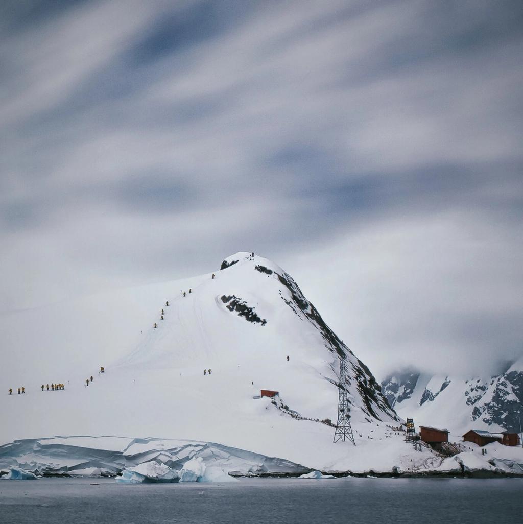 A line of tourists climbing a snowy mountain slope by the coast