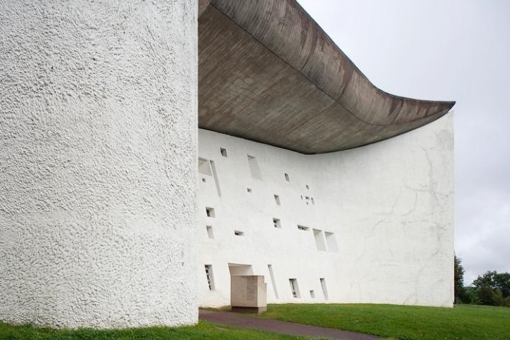 The white wall of the Chapelle Notre-Dame-du-Haut with varied window openings beneath the overhanging roof