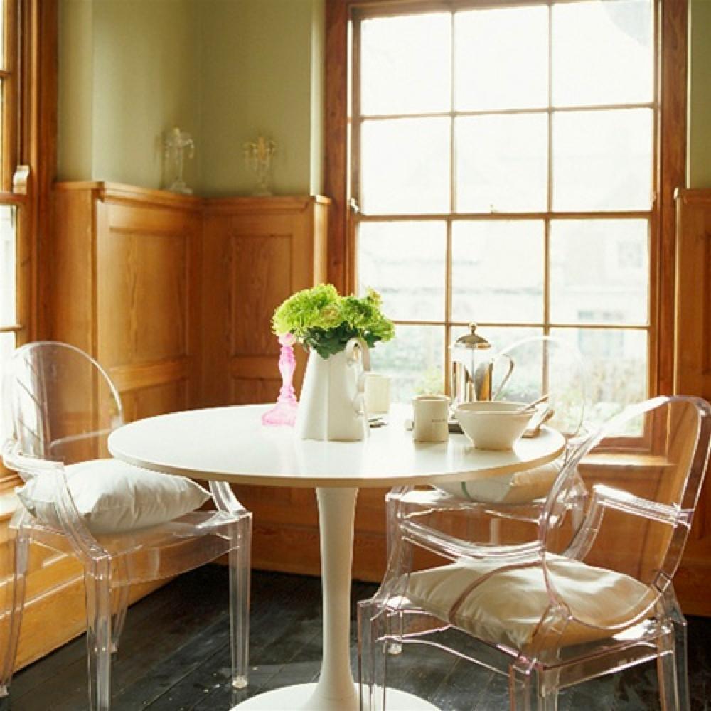 Two transparent Louis Ghost chairs at a white round table in an interior with wooden panelling