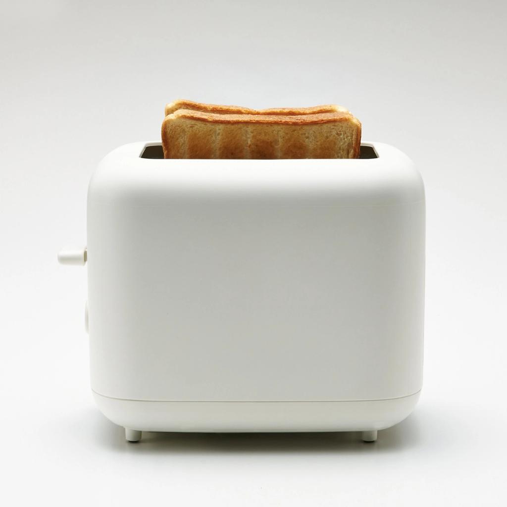 A white toaster viewed from the side, with toasted slices of bread protruding from the slot