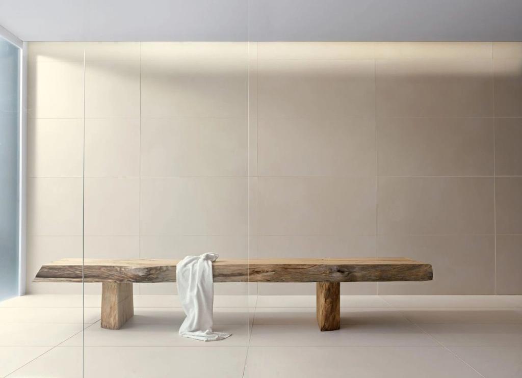 A solid-wood bench with a towel draped over it in a light-tiled interior