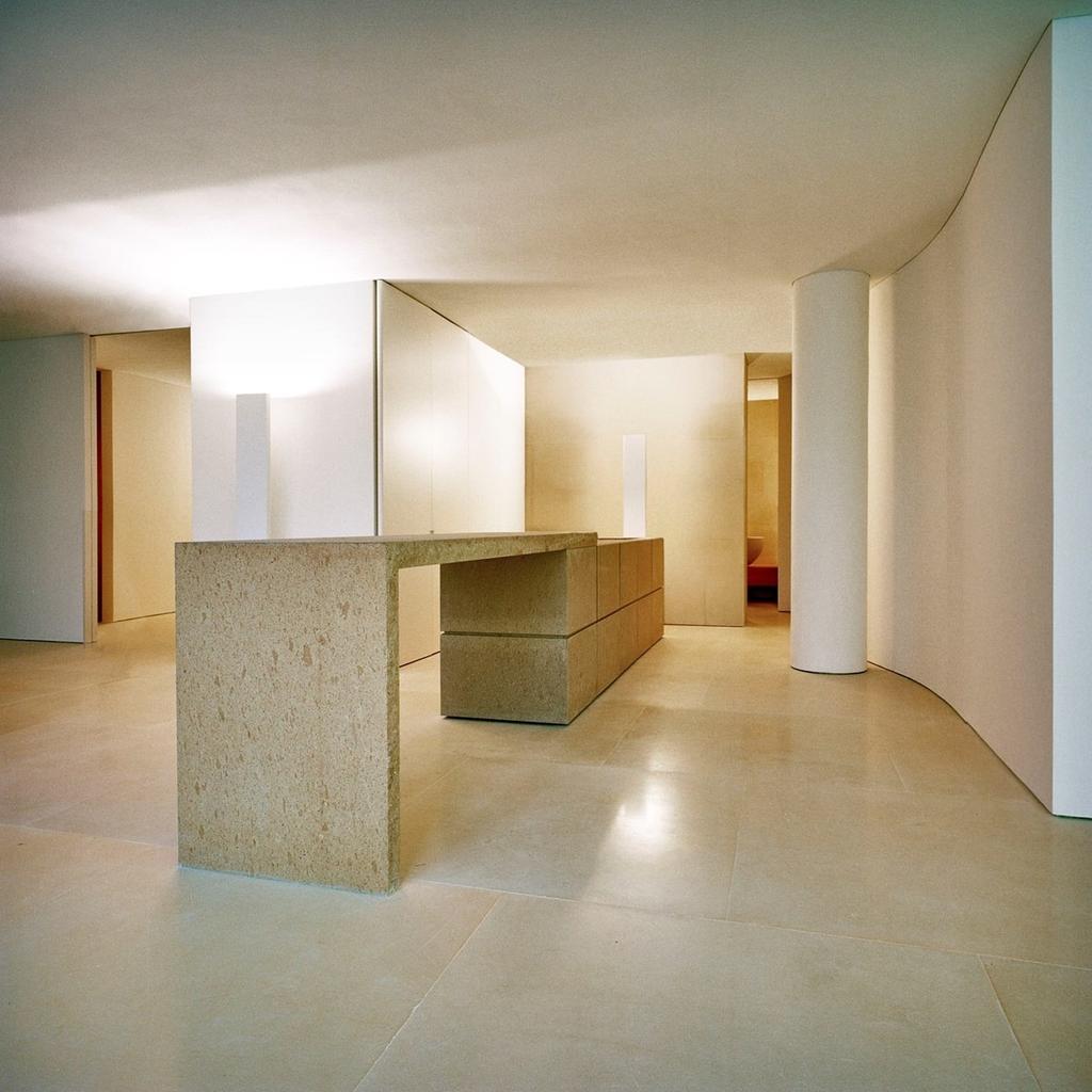 A spacious white hall with a stone console table and a curved wall — Silvestrin's minimalism