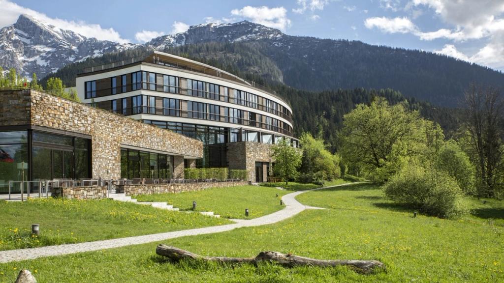 The curved building of Kempinski Berchtesgaden on a meadow at the foot of the Bavarian Alps