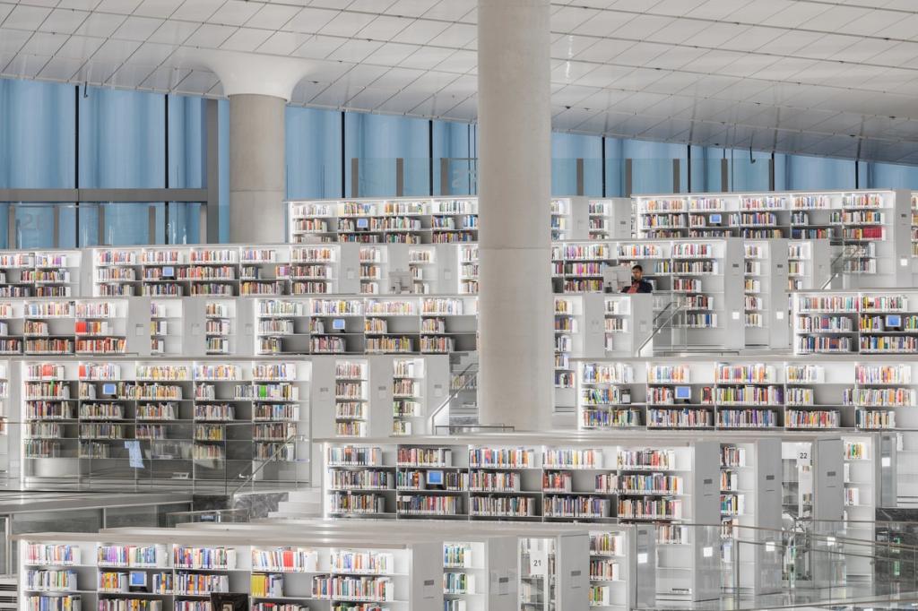 Белые ярусные книжные полки Национальной библиотеки Катара с круглой колонной и читателем