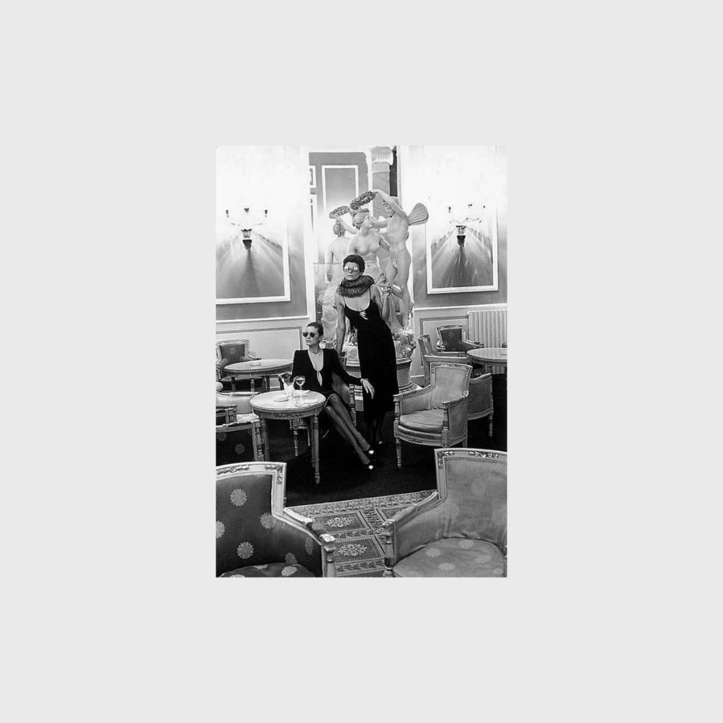 Two women in black evening gowns among antique furniture and sculptures in a grand salon