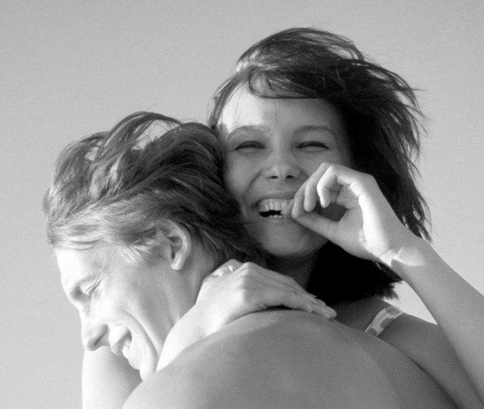 A young man and woman lie in the grass on sand, examining something up close