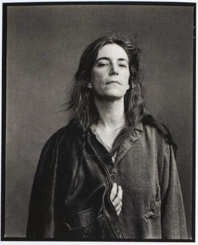 Portrait of singer Patti Smith with long hair in a worn jacket against a grey background