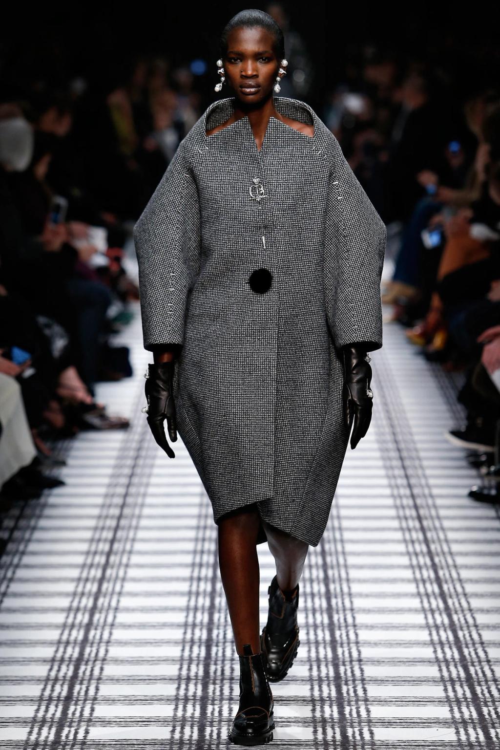 A grey Balenciaga tweed coat with open shoulders on a checked runway