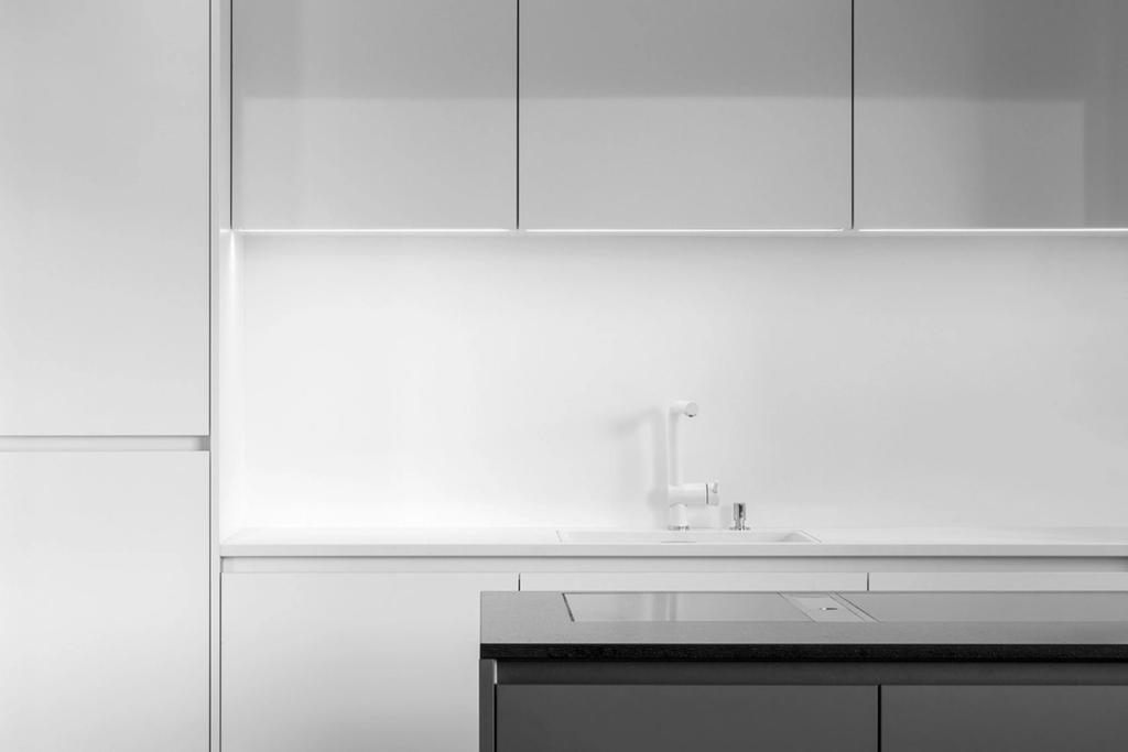 A minimalist white kitchen with white cabinetry and a dark island countertop