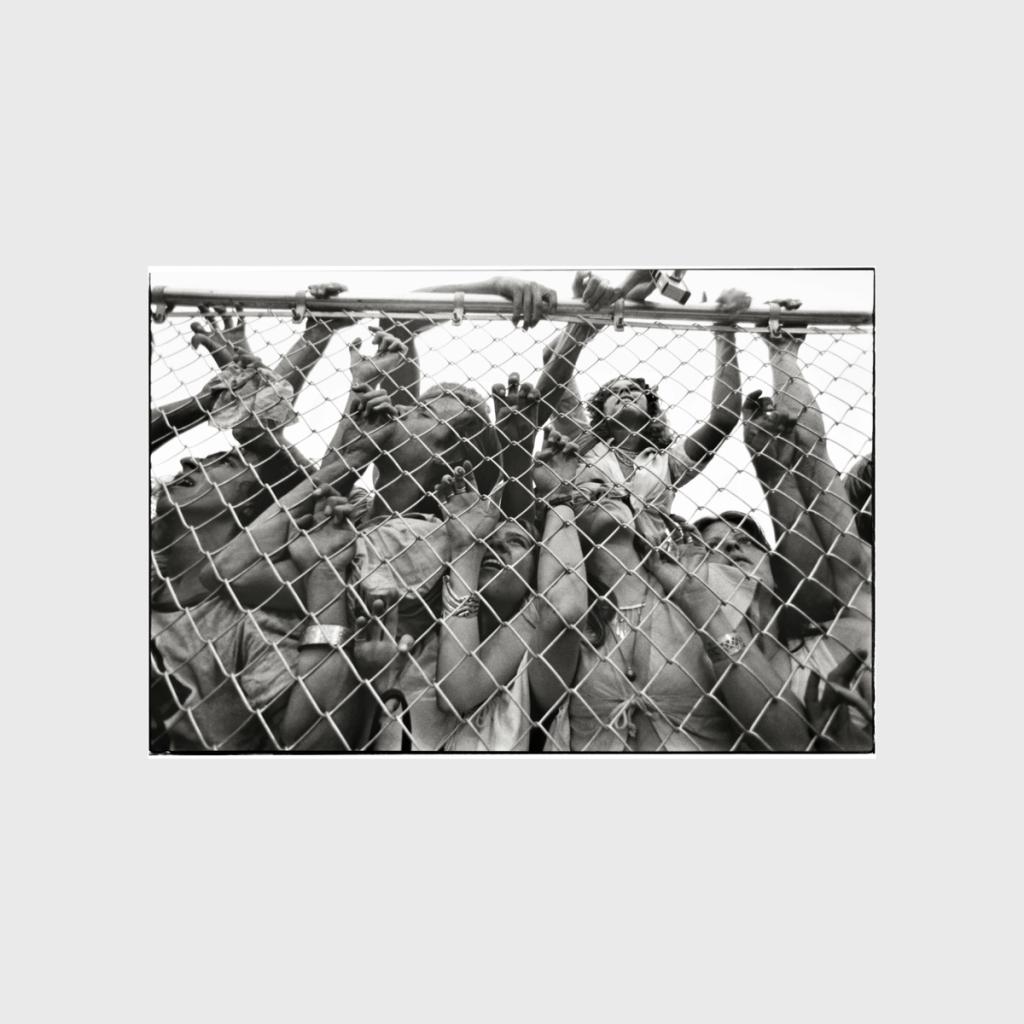 A black-and-white shot of a crowd of fans pressed against a mesh barrier at a concert