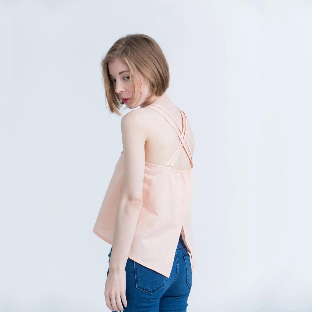 A girl seen from behind in a peach Kestan top with crossover straps and blue jeans