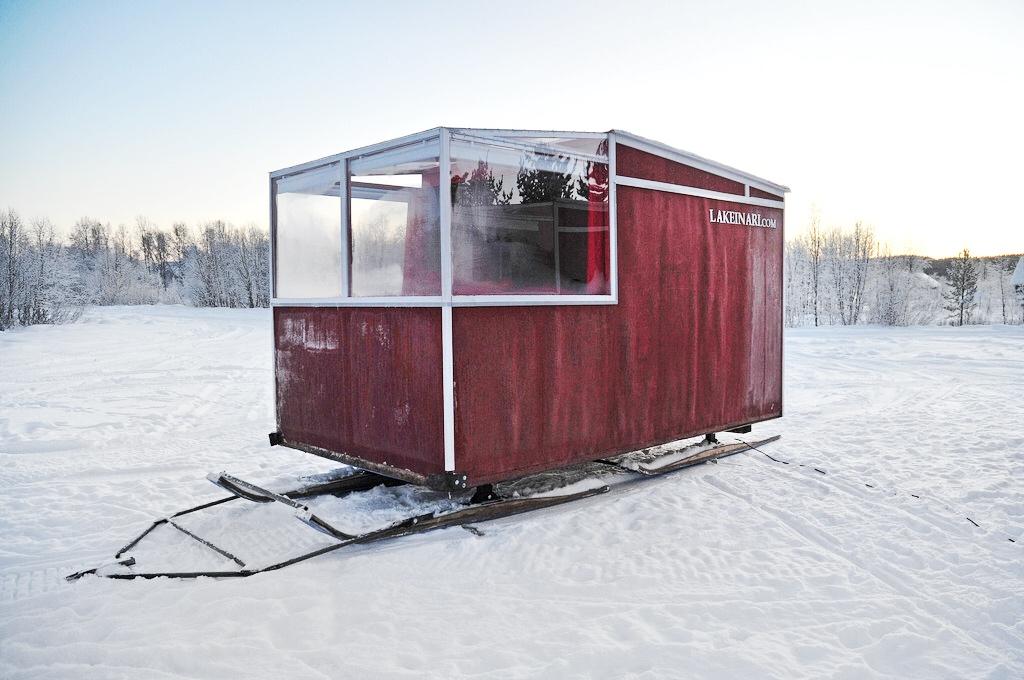 Красный передвижной домик Lake Inari на полозьях посреди заснеженной равнины