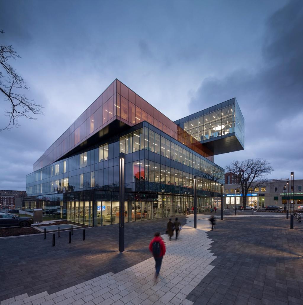 The glass Halifax library building with offset cantilevered volumes at dusk, passersby in the square