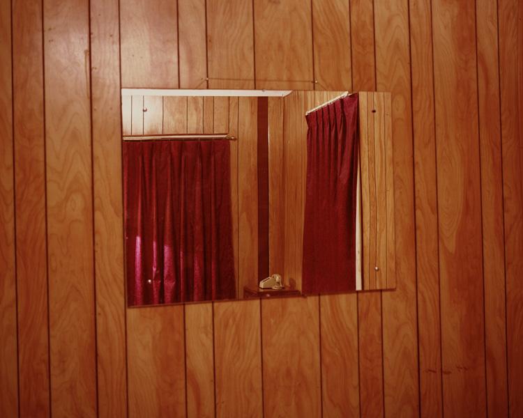 A rectangular mirror on a wood-panelled wall reflecting a window with red curtains