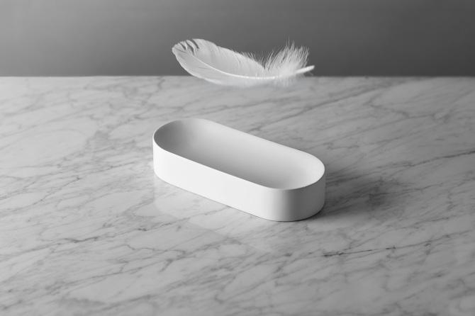 A white oval tray on a marble surface with a white feather floating above it, designed by Maxim Maximov