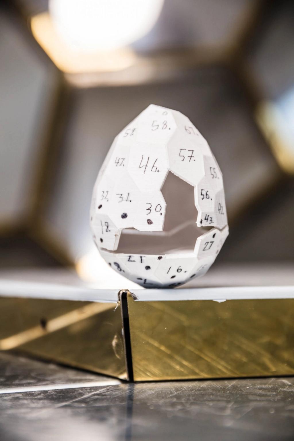 A white prototype of the Solar Egg with numbered facets, mounted on a brass stand