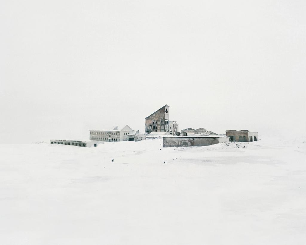 Ruins of stone structures with a pediment on a snow-covered wasteland beneath a white sky