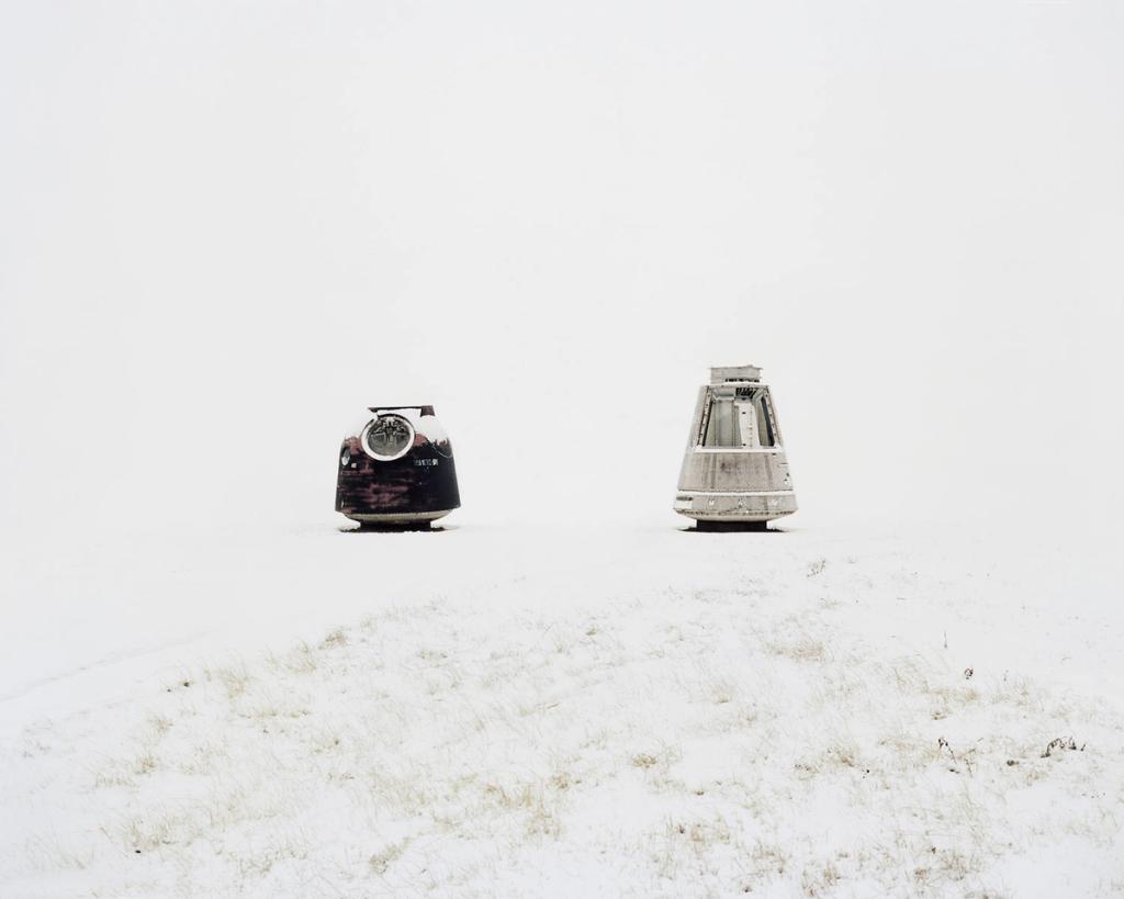 Two rusted descent modules from space capsules stand on a snow-covered hill
