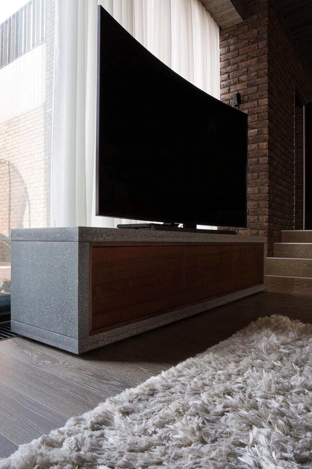 A curved television on a terrazzo and dark-wood unit set against a brick wall with a white curtain