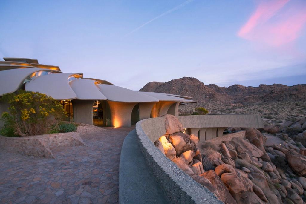 Дом с веерообразными бетонными сводами и каменной дорожкой в сумерках