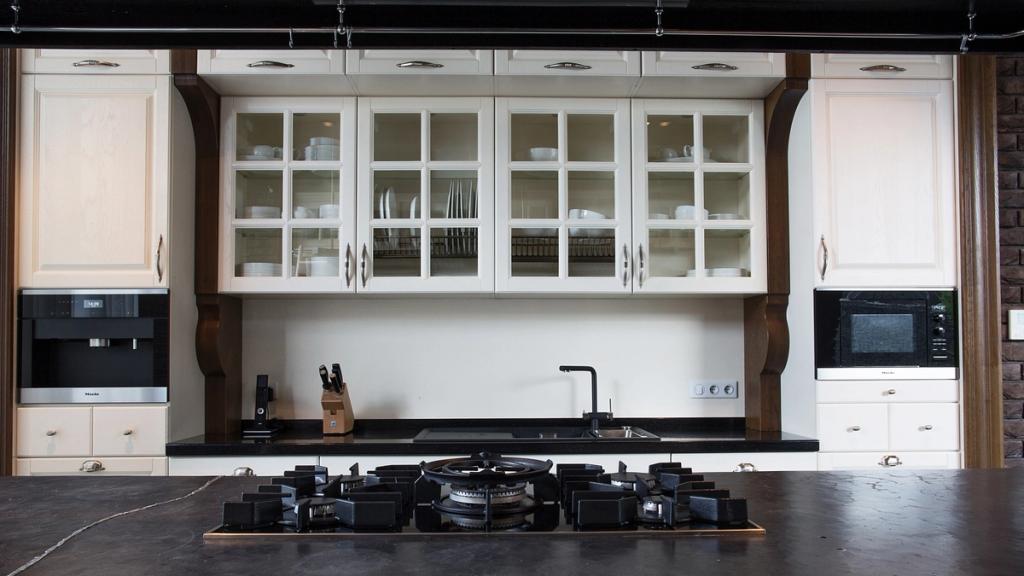 White kitchen cabinets with glass-fronted doors above a dark worktop with a gas hob