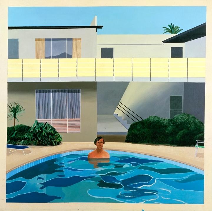 A man stands waist-deep in a pool against the backdrop of a two-storey Californian house