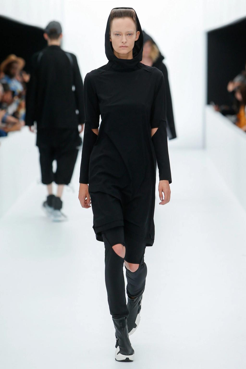 A Y-3 model in a black hooded dress and trainers on the runway