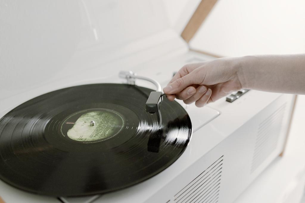 A hand lowers the tonearm and stylus onto a spinning vinyl record