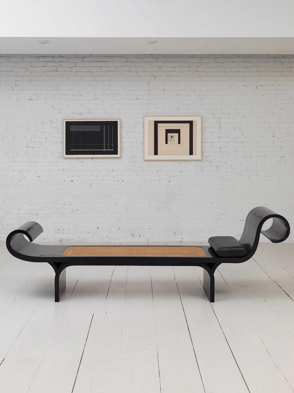 The black Marquesa daybed with a woven seat against a white brick wall