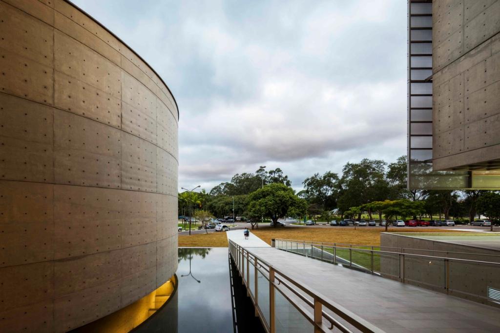 The cylindrical concrete volume of the Brasiliana Library beside a reflecting pool, with a pedestrian bridge leading to the building