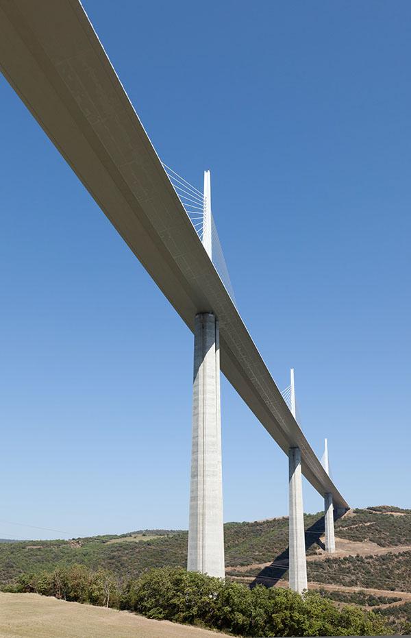 The Millau Viaduct at dusk: a row of tall pylons with stay cables above a green valley