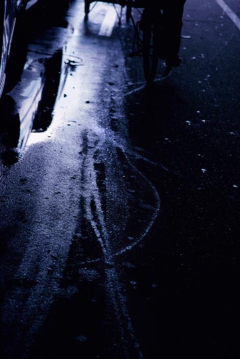 Wet night asphalt with reflections of light and the silhouette of a bicycle in blue tones