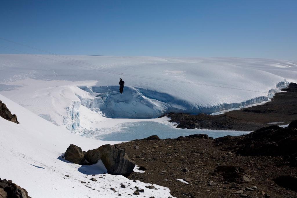 A person abseiling above a glacial crevasse filled with meltwater