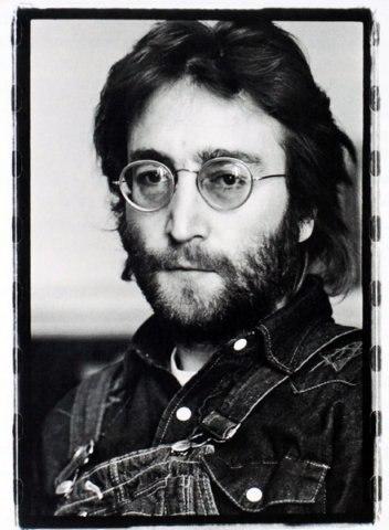 A close-up portrait of John Lennon in round glasses and a denim jacket