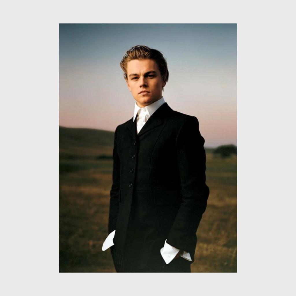 A colour portrait of a young Leonardo DiCaprio in a black suit, standing in a field at sunset