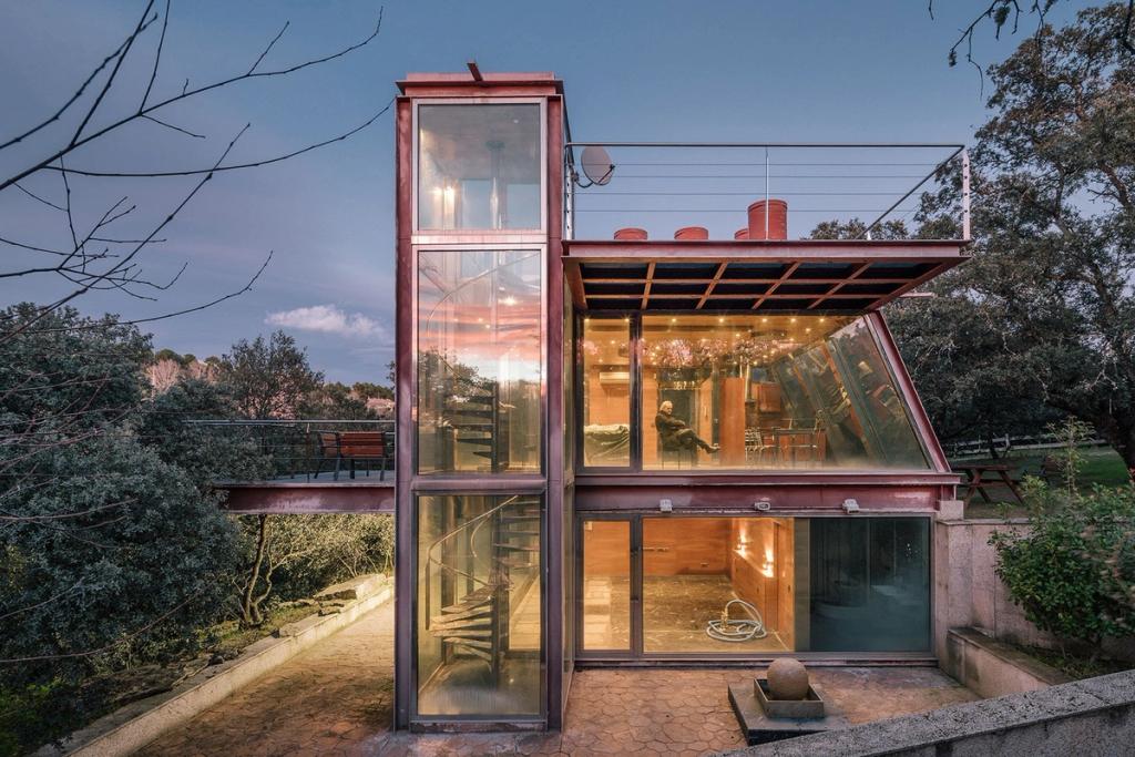 A glass-and-steel house with a spiral stair tower set among trees at dusk