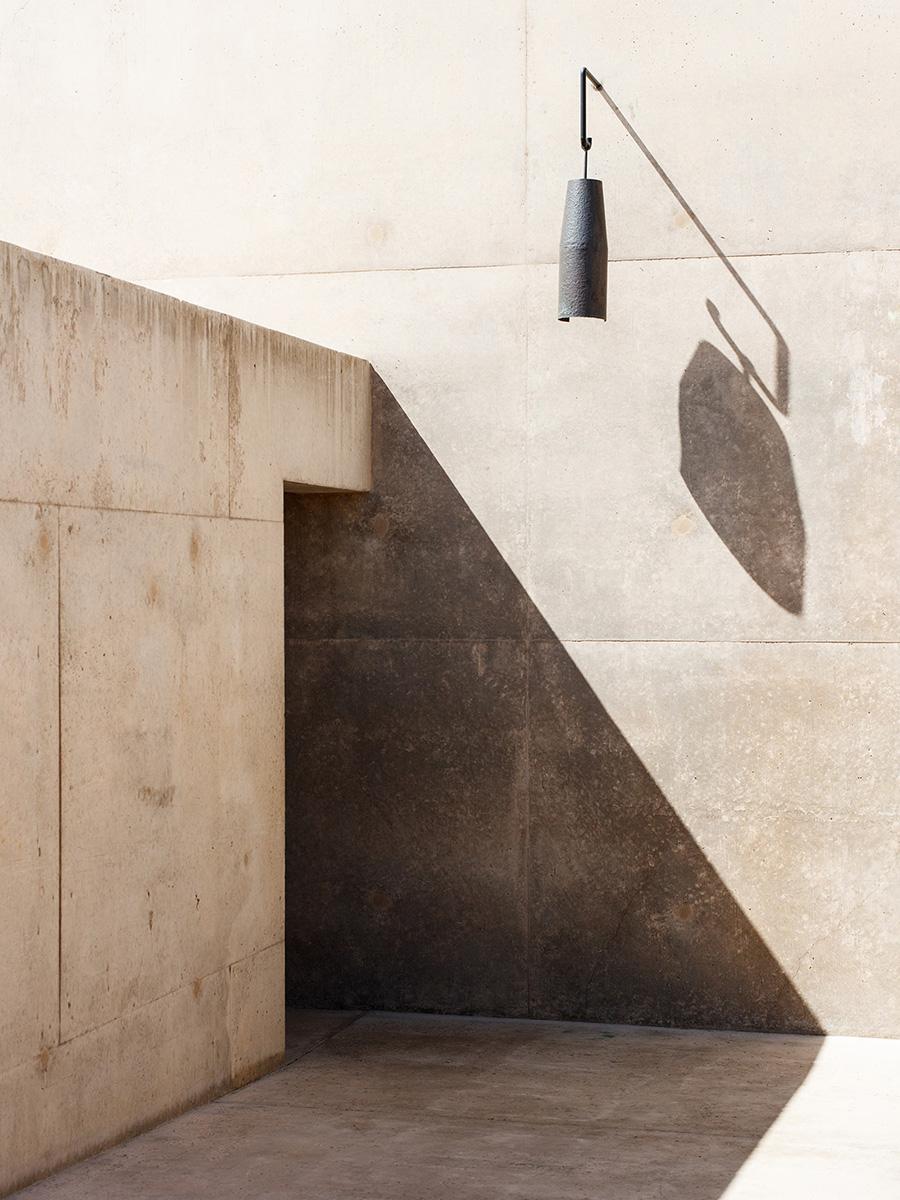 A dark ceramic pendant lamp casts shadows on a sun-drenched concrete wall at Amangiri
