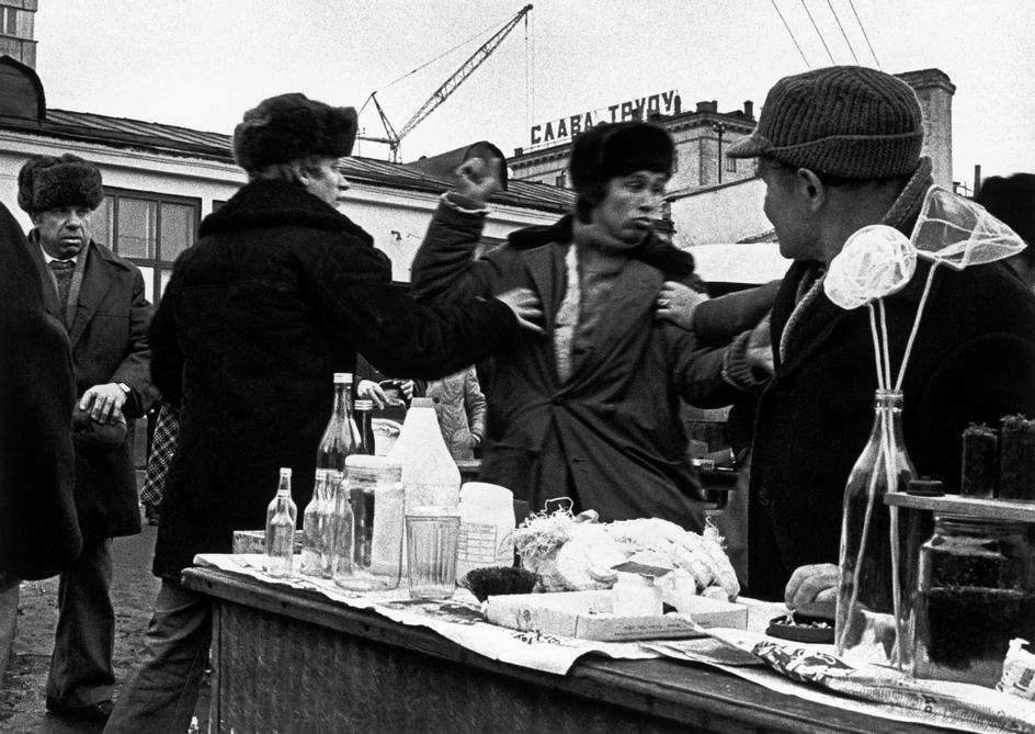 A street stall with bottles and food, people in winter hats arguing