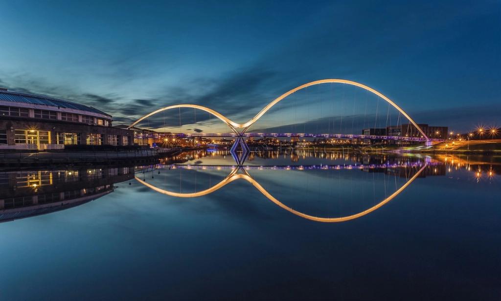 The Infinity Bridge at dusk: two arches in the shape of an infinity symbol reflected in calm water