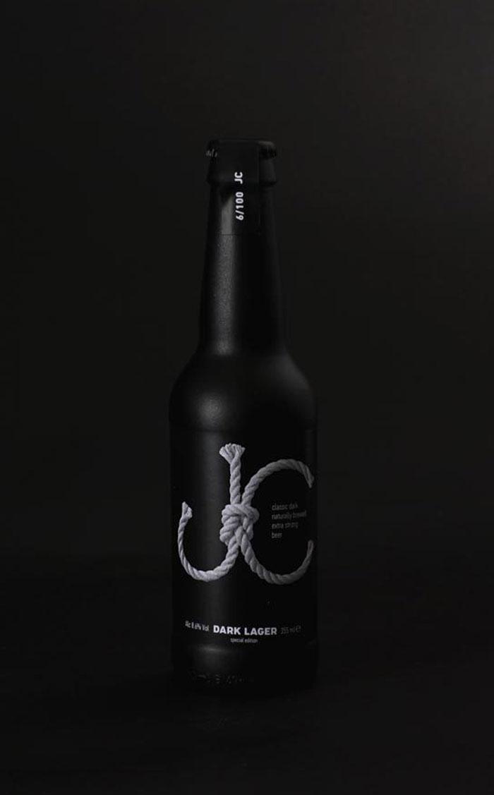 Чёрная бутылка пива JC Dark Lager с верёвочным логотипом на тёмном фоне
