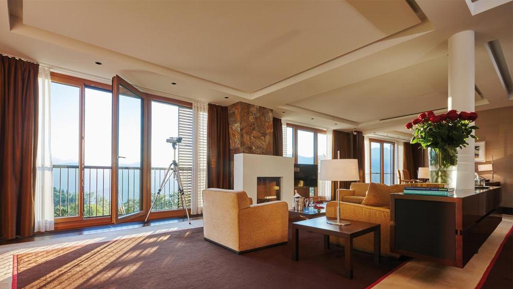 A spacious Kempinski suite with a fireplace, armchairs and panoramic mountain views