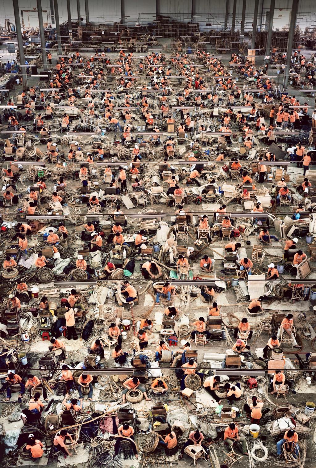 A factory floor from above: hundreds of workers in orange weave goods in rows