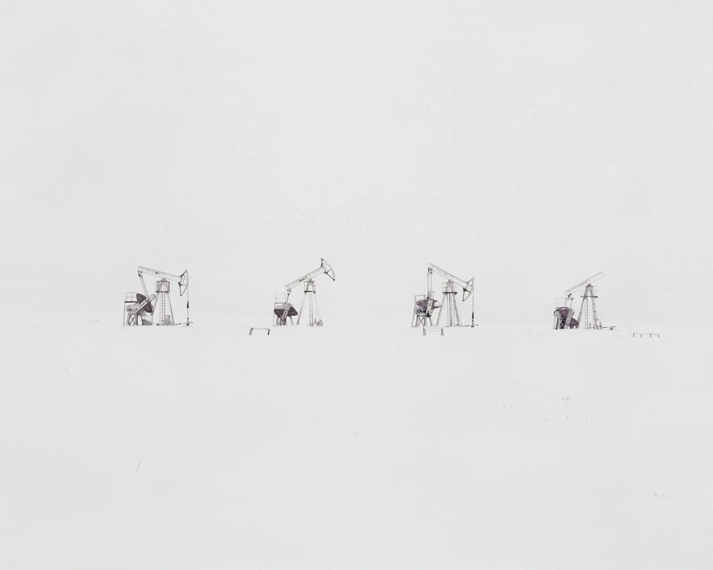 Four abandoned oil pump jacks lined up in a row on a white snowy plain