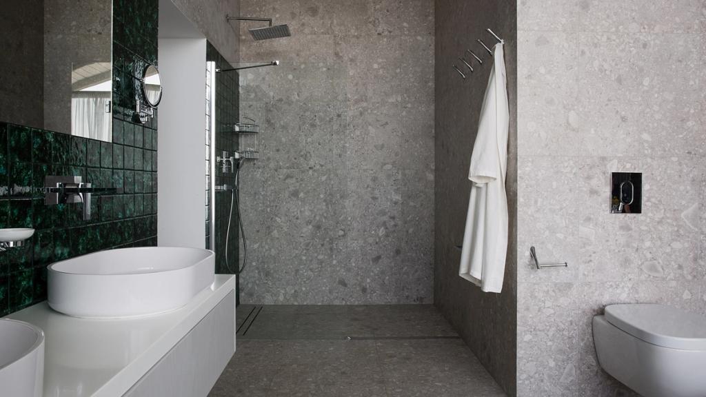 A bathroom with a shower zone, grey stone cladding and an accent wall of green tiles