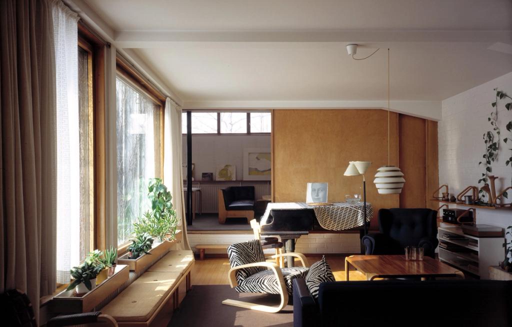 The living room of the Aalto house with large windows, planter boxes, Paimio armchairs and a grand piano