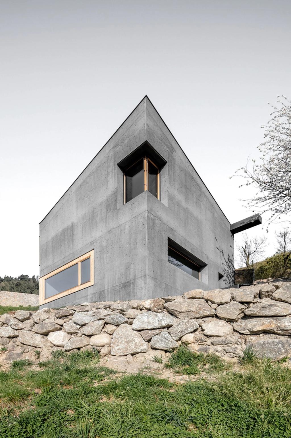 A corner of the Habitat Andergassen Urthaler concrete house, with timber-framed windows set above a stone base