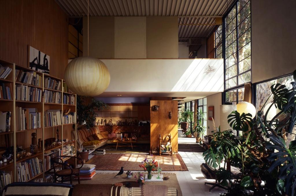 The double-height living room of the Eames House with shelving, plants and a globe pendant light