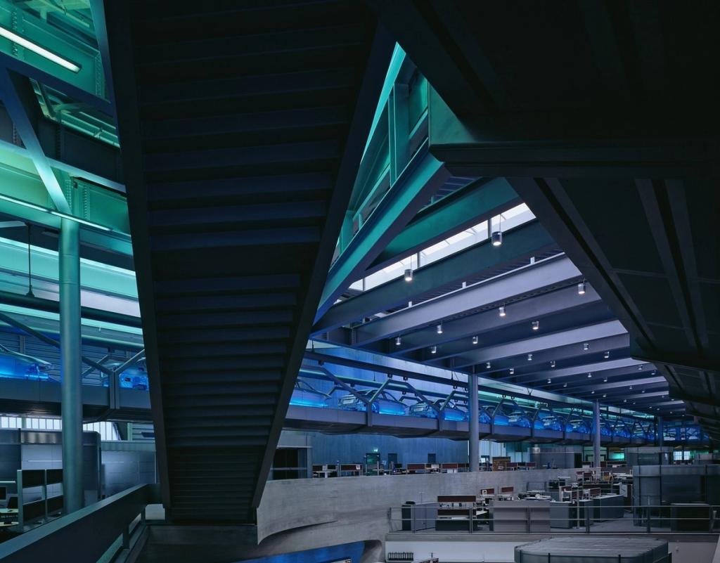 A dark tower with a spiralling atrium lit in green, rising above an elevated road at night